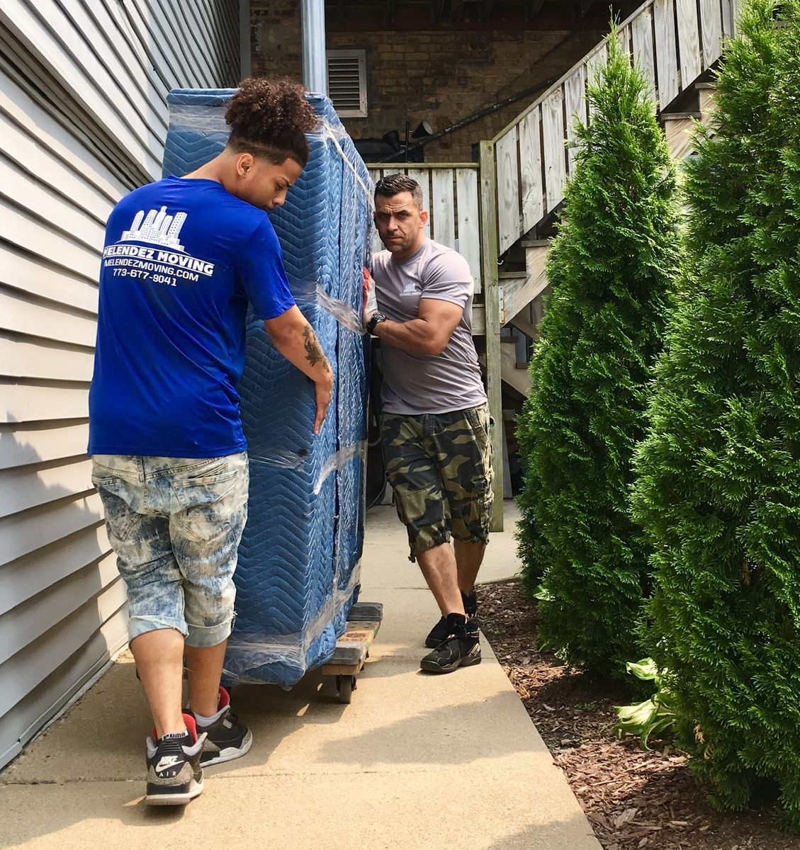 Uniformed Melendez Moving crew moving wrapped furniture on a dolly outside a Chicago home